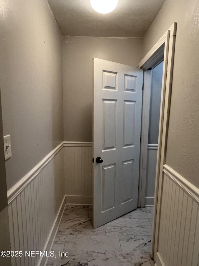 hallway featuring marble finish floor and wainscoting