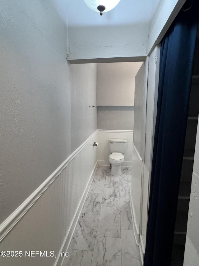 bathroom with a wainscoted wall, marble finish floor, and toilet