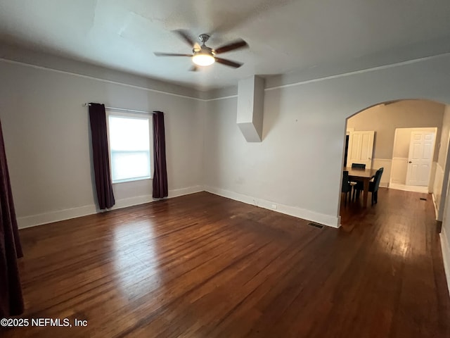 spare room with a ceiling fan, dark wood-style floors, arched walkways, and baseboards