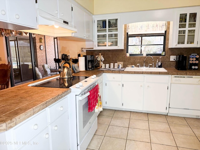 kitchen featuring a sink, backsplash, white appliances, white cabinets, and glass insert cabinets