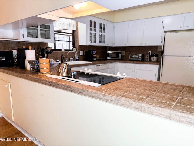 kitchen with freestanding refrigerator, a sink, decorative backsplash, glass insert cabinets, and stainless steel microwave