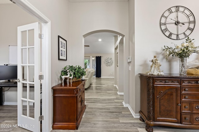 corridor featuring arched walkways, light wood-style flooring, and baseboards