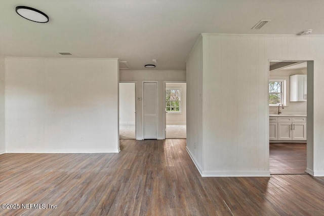 empty room featuring a sink, visible vents, baseboards, and wood finished floors