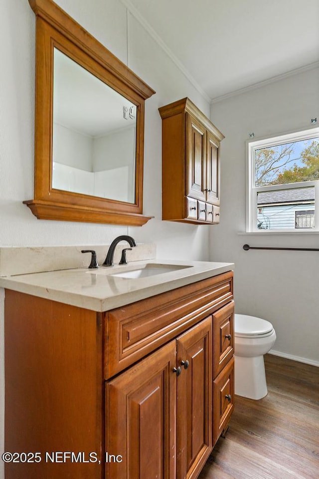 bathroom with baseboards, toilet, ornamental molding, wood finished floors, and vanity