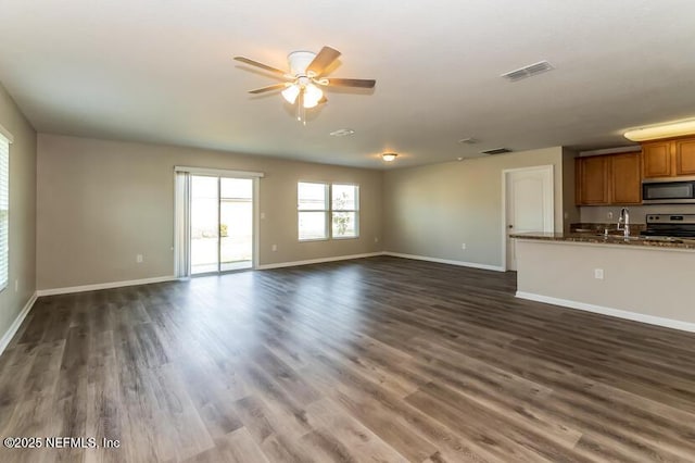 unfurnished living room with dark wood finished floors, visible vents, a ceiling fan, and baseboards