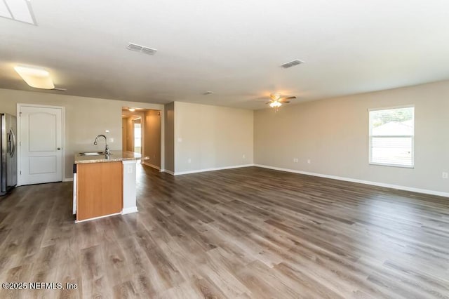 unfurnished living room with visible vents, a sink, baseboards, and dark wood-style flooring