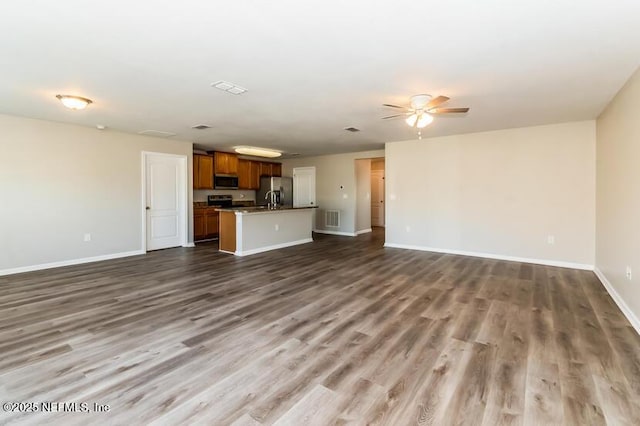 unfurnished living room featuring a ceiling fan, wood finished floors, baseboards, and visible vents