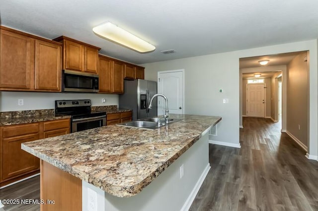 kitchen featuring visible vents, a sink, appliances with stainless steel finishes, brown cabinetry, and a kitchen island with sink