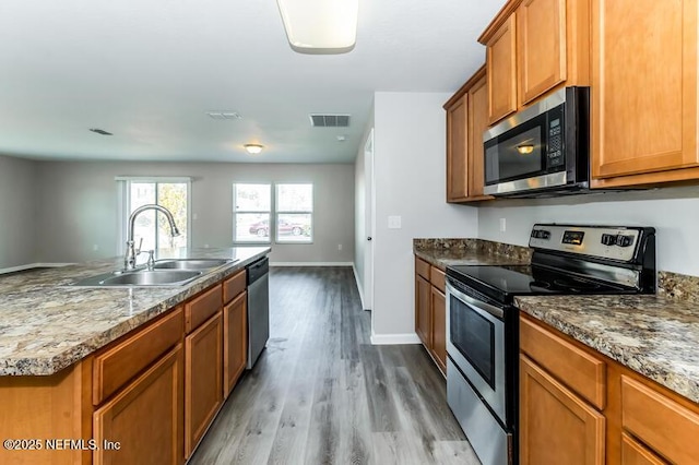 kitchen featuring visible vents, brown cabinets, a sink, wood finished floors, and appliances with stainless steel finishes