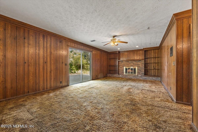 unfurnished living room with a brick fireplace, built in shelves, wood walls, and carpet floors