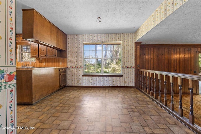 kitchen with baseboards, a textured ceiling, wallpapered walls, and brick floor