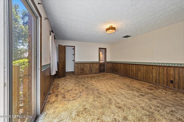 carpeted spare room with visible vents, wallpapered walls, wainscoting, wood walls, and a textured ceiling