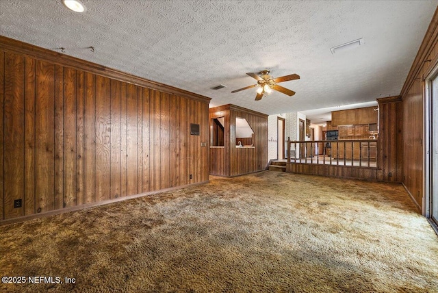 unfurnished living room with wooden walls, visible vents, a textured ceiling, crown molding, and carpet flooring