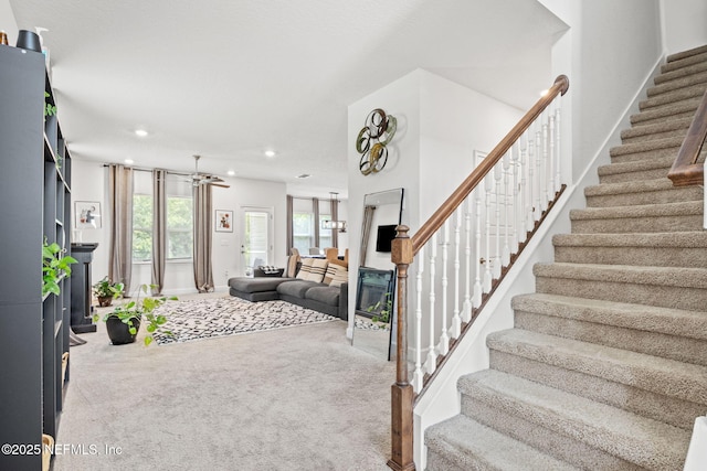 living room with stairs, a glass covered fireplace, and carpet flooring