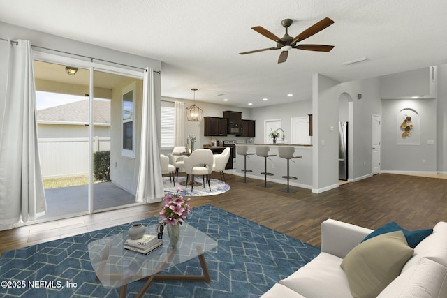 living area with arched walkways, baseboards, ceiling fan, and wood finished floors