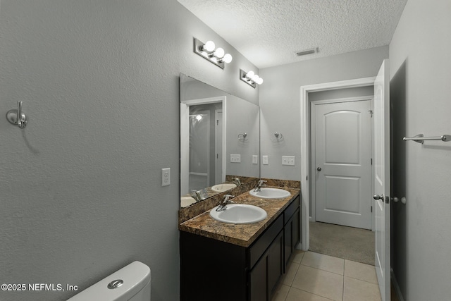 bathroom featuring a textured ceiling, toilet, visible vents, and a sink