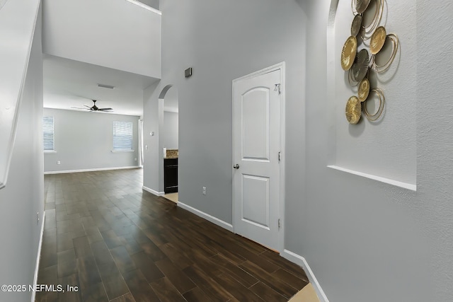 hallway featuring dark wood finished floors, baseboards, and arched walkways