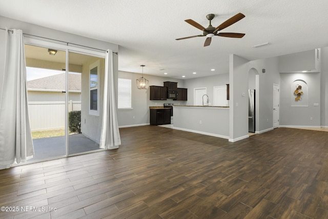 unfurnished living room featuring baseboards, ceiling fan, arched walkways, dark wood-style floors, and a sink