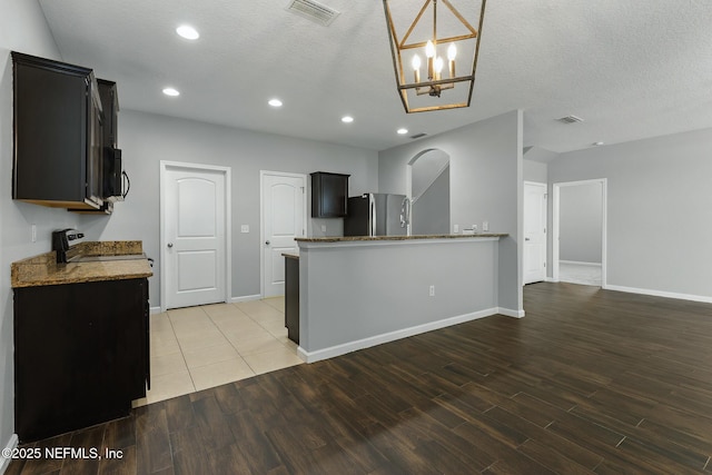 kitchen with light wood finished floors, light stone counters, visible vents, and freestanding refrigerator