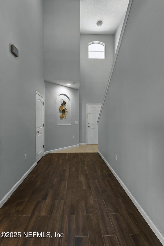 unfurnished living room with baseboards, wood finished floors, and a towering ceiling