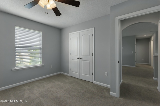 unfurnished bedroom with baseboards, arched walkways, a textured ceiling, and carpet flooring