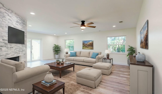 living room with recessed lighting, a stone fireplace, a healthy amount of sunlight, and light wood-type flooring