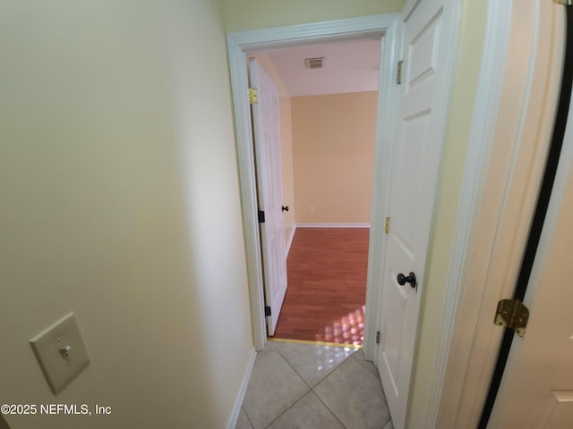 hallway with light tile patterned floors, visible vents, and baseboards