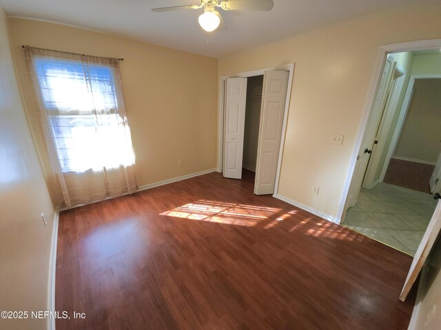 unfurnished bedroom featuring wood finished floors, baseboards, and a closet