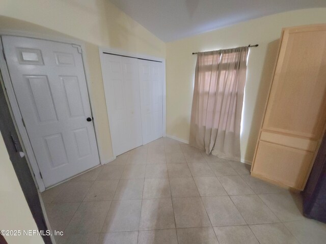 unfurnished bedroom with vaulted ceiling, light tile patterned floors, baseboards, and a closet