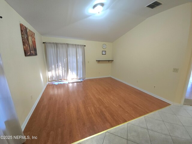 tiled empty room with visible vents, baseboards, and lofted ceiling