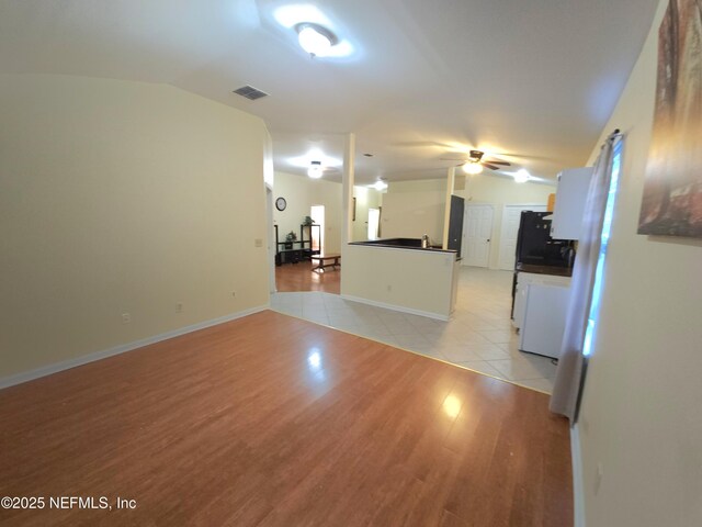 unfurnished living room featuring visible vents, baseboards, light wood-type flooring, lofted ceiling, and a ceiling fan