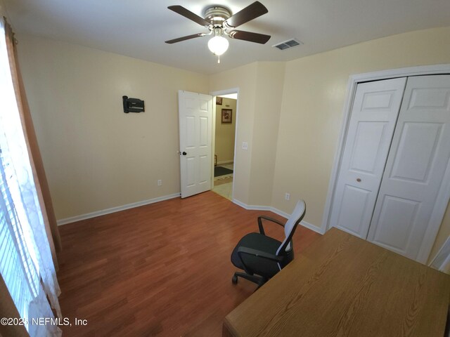 unfurnished office featuring ceiling fan, visible vents, baseboards, and wood finished floors