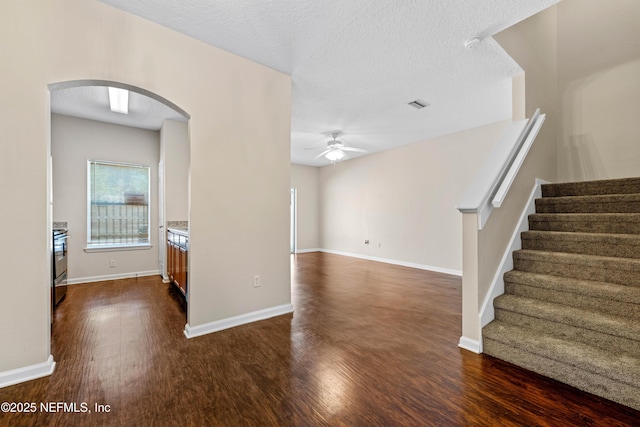 interior space with visible vents, baseboards, arched walkways, a ceiling fan, and dark wood-style flooring