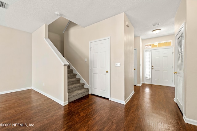 foyer entrance with visible vents, a textured ceiling, wood finished floors, baseboards, and stairs