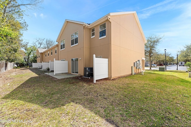 rear view of house featuring fence, a yard, central AC, stucco siding, and a patio area