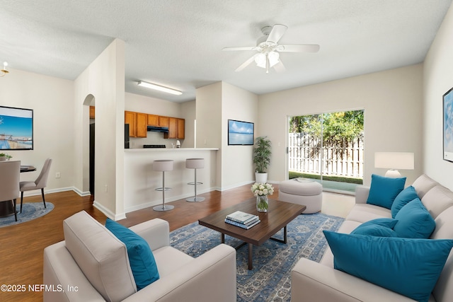 living area featuring a ceiling fan, a textured ceiling, dark wood-style floors, arched walkways, and baseboards