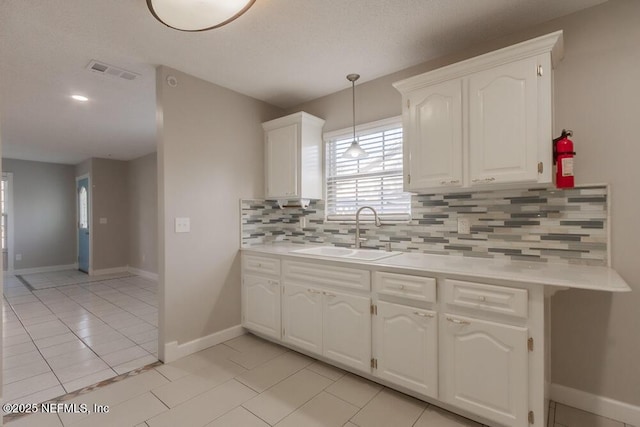 kitchen with visible vents, light tile patterned floors, decorative backsplash, white cabinets, and a sink