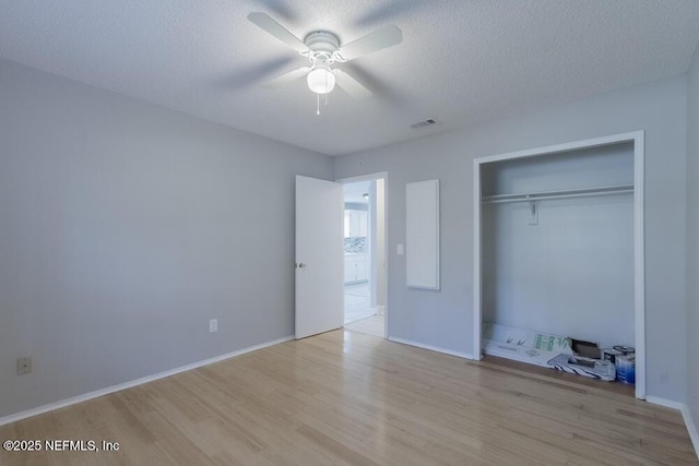 unfurnished bedroom featuring a textured ceiling, a closet, light wood-style floors, baseboards, and ceiling fan