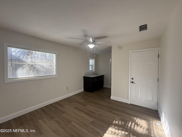 unfurnished room featuring a wealth of natural light, baseboards, dark wood-style floors, and ceiling fan