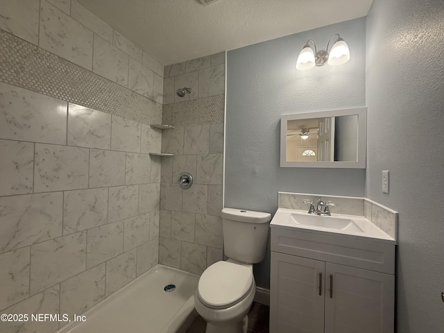 bathroom featuring vanity, toilet, a textured wall, and tiled shower