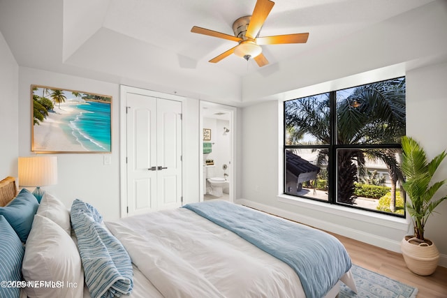 bedroom with a tray ceiling, baseboards, a closet, and wood finished floors