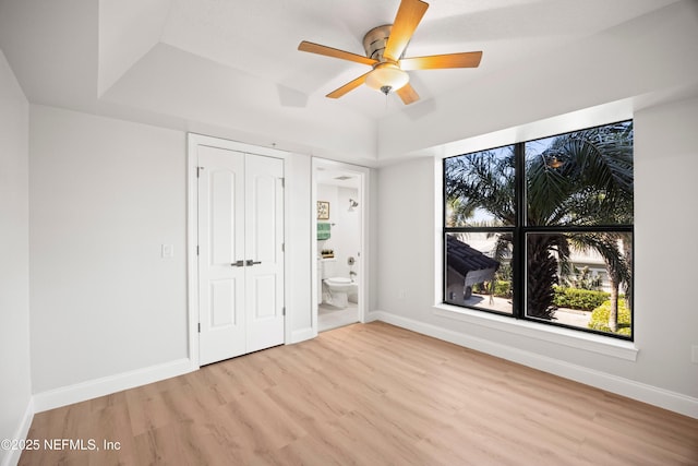 unfurnished bedroom with a tray ceiling, baseboards, wood finished floors, and ensuite bathroom