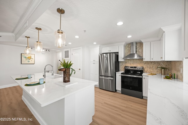 kitchen with white cabinets, light wood-style floors, appliances with stainless steel finishes, wall chimney range hood, and backsplash