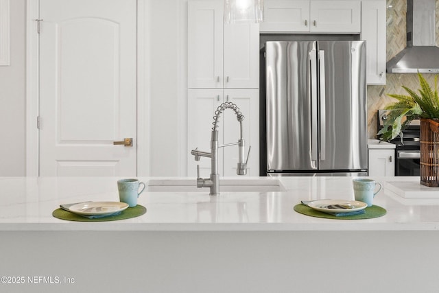 interior details featuring appliances with stainless steel finishes, white cabinets, light countertops, and wall chimney range hood