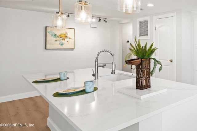 kitchen featuring light stone counters, baseboards, light wood finished floors, a sink, and hanging light fixtures