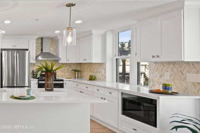 kitchen featuring appliances with stainless steel finishes, white cabinetry, light countertops, and wall chimney range hood