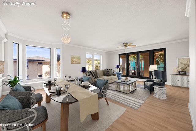 living room with ceiling fan with notable chandelier, crown molding, baseboards, and wood finished floors