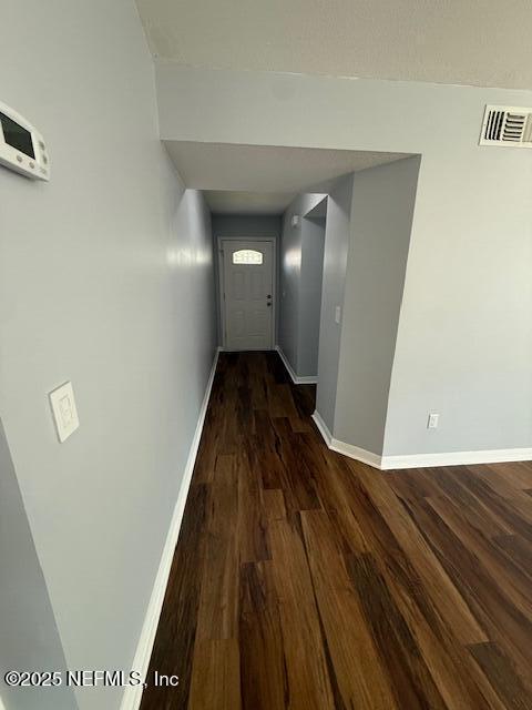 hall with visible vents, baseboards, and wood finished floors