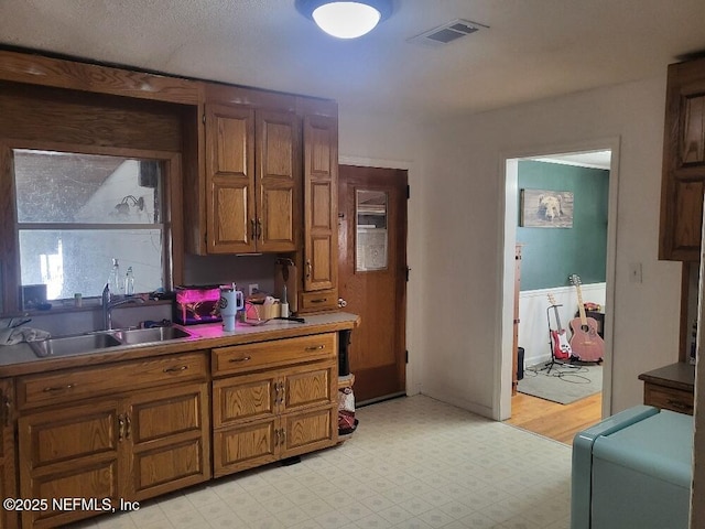 kitchen featuring brown cabinets, light floors, visible vents, and a sink