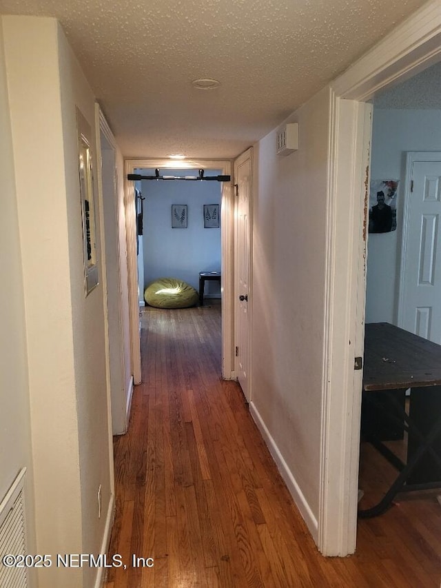 corridor featuring wood finished floors, baseboards, and a textured ceiling